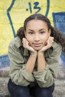Porträt eines Teenagers mit dem Kopf in den Händen vor einem Graffiti sitzend - OJF000159
