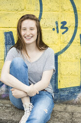 Porträt eines lachenden Teenagers mit Zahnspange, der vor einem Graffiti sitzt - OJF000161