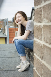 Lachendes Teenager-Mädchen mit Zahnspange auf dem Dach sitzend - OJF000163