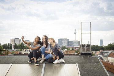 Deutschland, Berlin, drei Freunde sitzen nebeneinander auf dem Dach und machen ein Selfie mit Smartphone - OJF000172