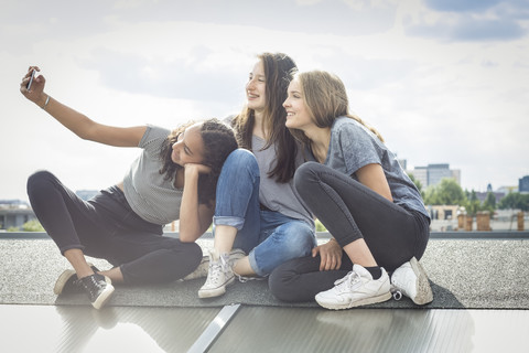 Germany, Berlin, three friends sitting on roof top taking selfie with smartphone stock photo