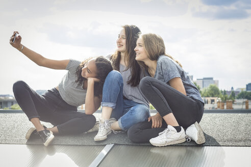 Deutschland, Berlin, drei Freunde sitzen auf dem Dach und machen ein Selfie mit Smartphone - OJF000173