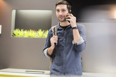 Mann mit Rucksack im Büro telefoniert mit Handy - ZEF009699