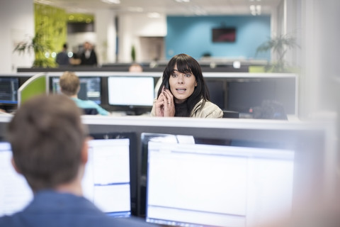 Frau am Telefon im Büro mit Blick auf einen Kollegen, lizenzfreies Stockfoto