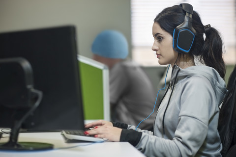 Junge Frau mit Kopfhörern bei der Arbeit am Computer in einer Bürozelle, lizenzfreies Stockfoto