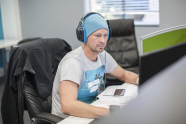 Junger Mann mit Kopfhörern bei der Arbeit am Computer im Büro - ZEF009730