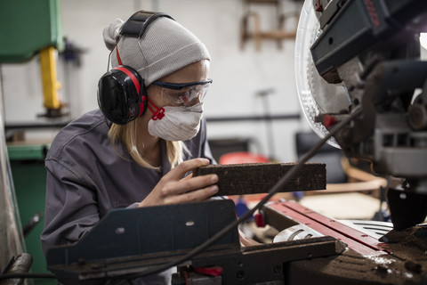 Frau mit Gehörschutz und Staubmaske bei der Arbeit an einer Maschine, lizenzfreies Stockfoto