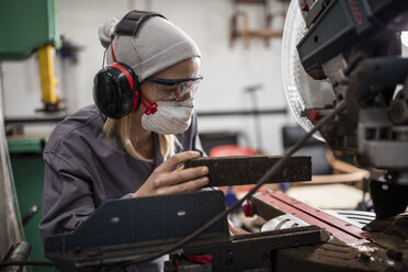 Frau mit Gehörschutz und Staubmaske bei der Arbeit an einer Maschine - ZEF009751