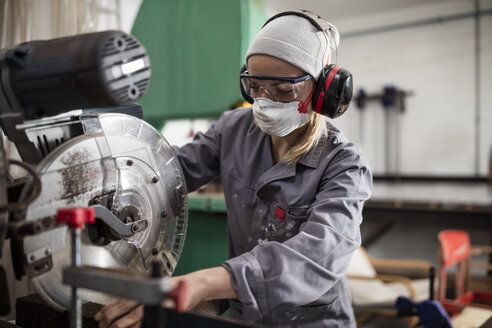 Frau mit Gehörschutz und Staubmaske bei der Arbeit an einer Maschine - ZEF009753