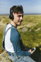 Entspannter junger Mann, der mit drahtlosen Kopfhörern in der Natur Musik hört - BOYF000530