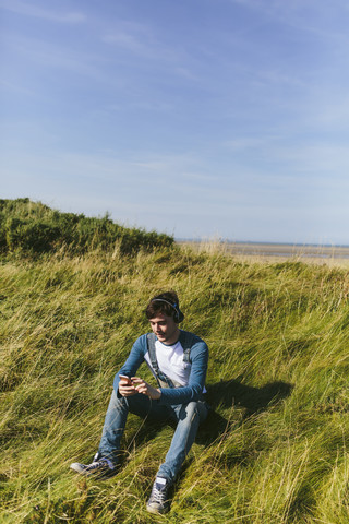 Entspannter junger Mann, der mit drahtlosen Kopfhörern in der Natur Musik hört, lizenzfreies Stockfoto
