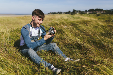 Lächelnder junger Mann sitzt auf einer Wiese und schaut in die Kamera, lizenzfreies Stockfoto