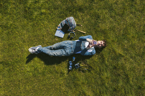 Entspannter junger Mann liegt auf einer Wiese und benutzt sein Handy, Draufsicht - BOYF000541