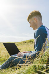 Junger Mann sitzt auf einer Wiese und benutzt einen Laptop - BOYF000542