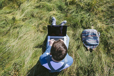 Draufsicht auf einen jungen Mann, der auf einer Wiese sitzt und einen Laptop benutzt - BOYF000543