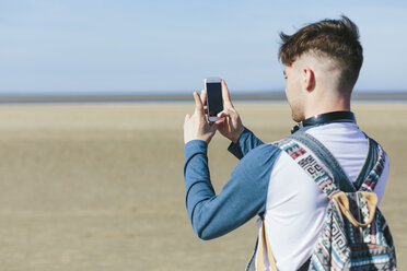 Junger Mann fotografiert mit Smartphone am Strand - BOYF000554