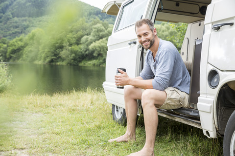 Lächelnder Mann sitzt in einem Lieferwagen am Seeufer, lizenzfreies Stockfoto