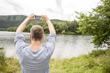 Man taking a cell phone picture at lakeside - FMKF002785