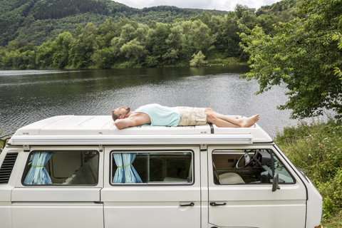 Mann auf dem Dach eines Lieferwagens am Seeufer liegend, lizenzfreies Stockfoto