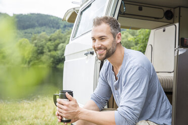 Smiling man sitting in a van at lakeside - FMKF002788