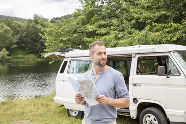 Man holding map at a van at lakeside - FMKF002790
