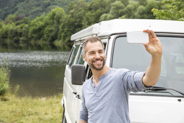 Lächelnder Mann macht ein Selfie mit einem Lieferwagen am Seeufer - FMKF002798