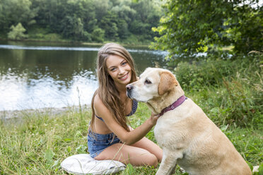 Junge Frau mit ihrem Hund am Seeufer sitzend - FMKF002813