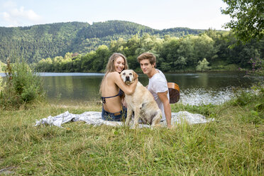 Junges Paar mit Hund sitzt am Seeufer - FMKF002816