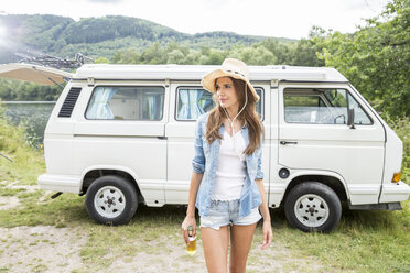 Woman wearing hat walking with beer bottle beside van - FMKF002820