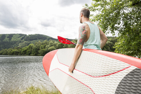 Mann mit Stand Up Paddle Board am Seeufer - FMKF002823