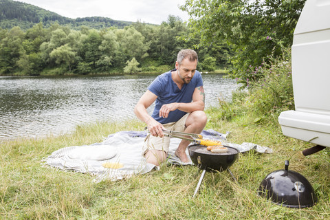 Mann beim Grillen am Seeufer, lizenzfreies Stockfoto