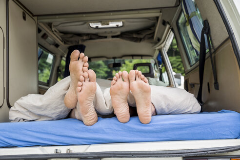 Feet of a couple lying on mattress in van - FMKF002856