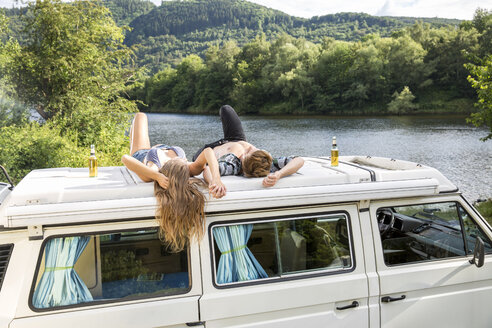 Young couple lying on roof of a van at lakeside - FMKF002862