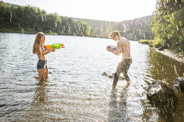 Young couple in a lake splashing with waterguns - FMKF002875