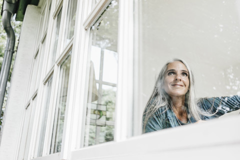 Smiling woman at home looking through window stock photo