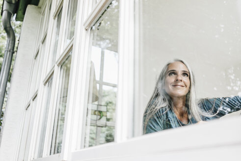 Smiling woman at home looking through window - KNSF000268
