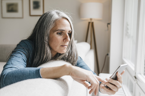 Frau sitzt auf der Couch und schaut auf ihr Handy, lizenzfreies Stockfoto