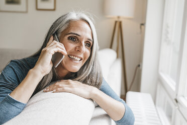 Smiling woman sitting on the couch telephoning with cell phone - KNSF000276