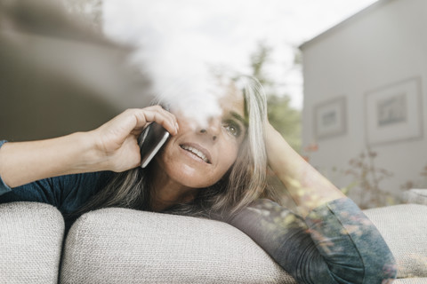 Woman on the phone sitting behind windowpane on the couch looking at distance stock photo