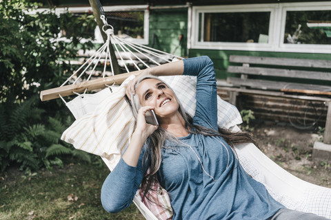 Frau am Telefon liegend in Hängematte im Garten, lizenzfreies Stockfoto