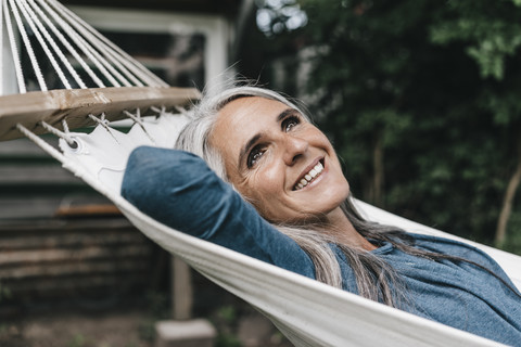 Porträt einer lächelnden Frau, die in einer Hängematte im Garten liegt, lizenzfreies Stockfoto