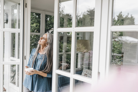Nachdenkliche Frau lehnt an der Tür ihres Wintergartens, lizenzfreies Stockfoto