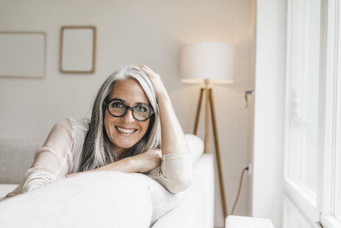 Porträt einer lächelnden Frau, die zu Hause auf der Couch sitzt - KNSF000300