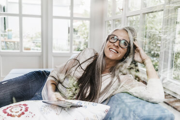 Portrait of smiling woman with e-book lying on lounge in her winter garden - KNSF000301