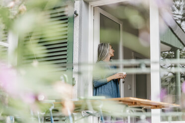 Frau lehnt mit einer Tasse Kaffee an der Terrassentür - KNSF000311