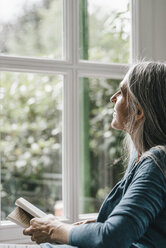 Woman with book looking through window - KNSF000319