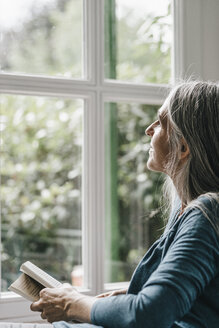 Frau mit Buch schaut durch das Fenster - KNSF000319