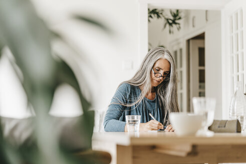 Portrait of woman sitting at table writing down something - KNSF000328