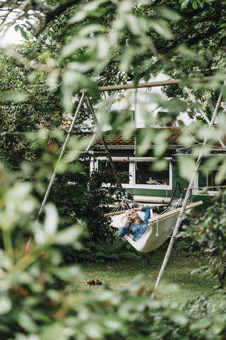 Frau am Telefon entspannt sich in der Hängematte im Garten, lizenzfreies Stockfoto