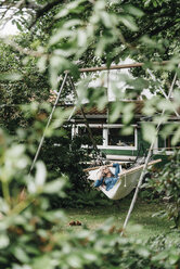 Woman on the phone relaxing in hammock in the garden - KNSF000335